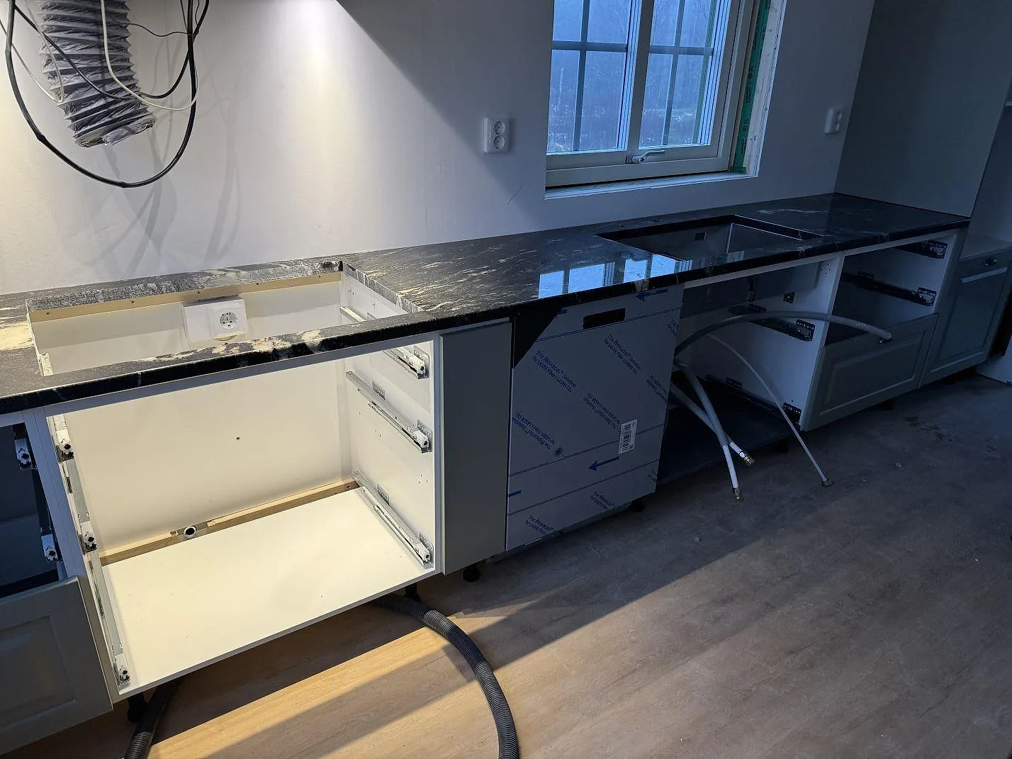 Väggbänk i polerad Cosmic Black granit med synliga urtag och öppna köksstommar i Älmhult.