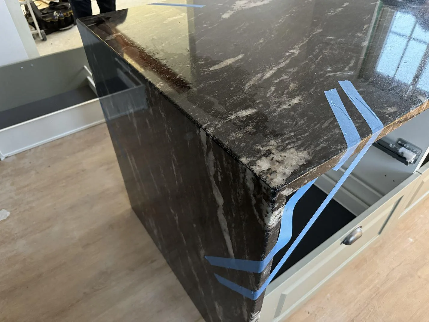 Närbild på polerad Cosmic Black granit med ljus ådring och tejpade kanter på en köksö i Älmhult.