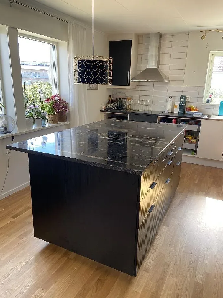 Köksö i svart granit Cosmic Black med grå och vit ådring, polerad, installerad i ett ljust kök i Båstad.