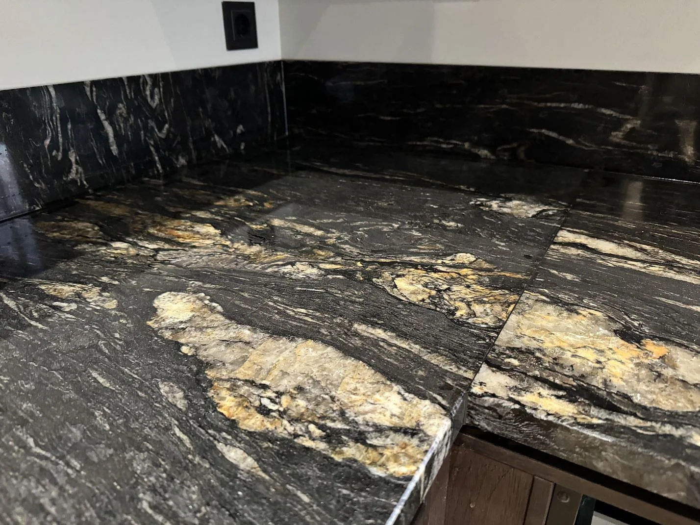 Hörndetalj av polerad Cosmic Black granit som köksbänkskiva med markerad ljus ådring och stänkskydd i Grebbestad.