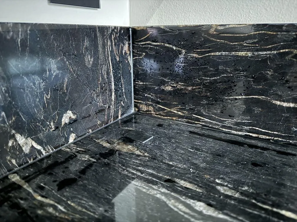 Närbild på uppvikt stänkskydd och köksbänkskiva i polerad Cosmic Black granit under montering i Grebbestad.