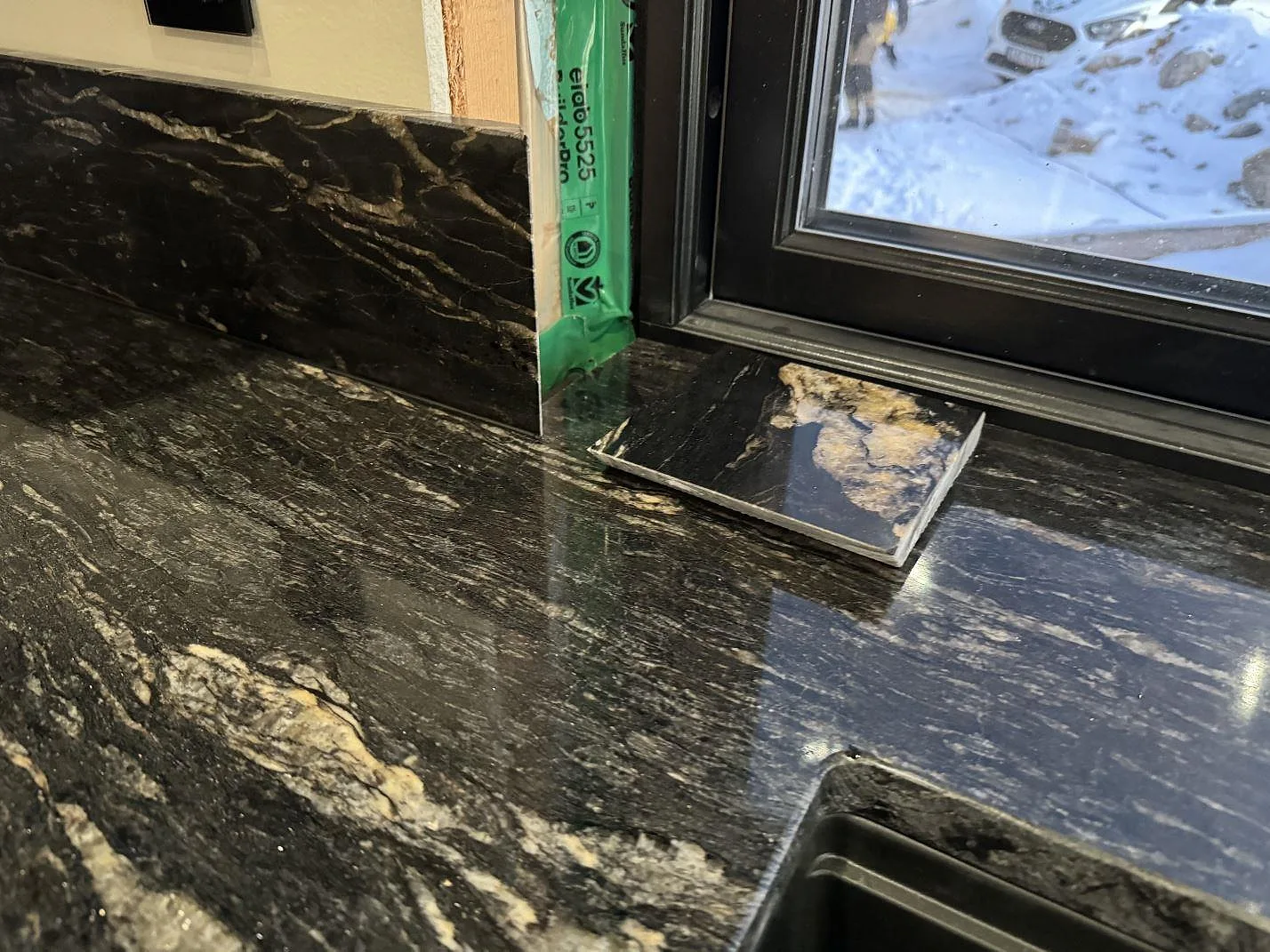 Detalj vid fönster med polerad Cosmic Black granit, stänkskydd och diskhozon under montering i Grebbestad.