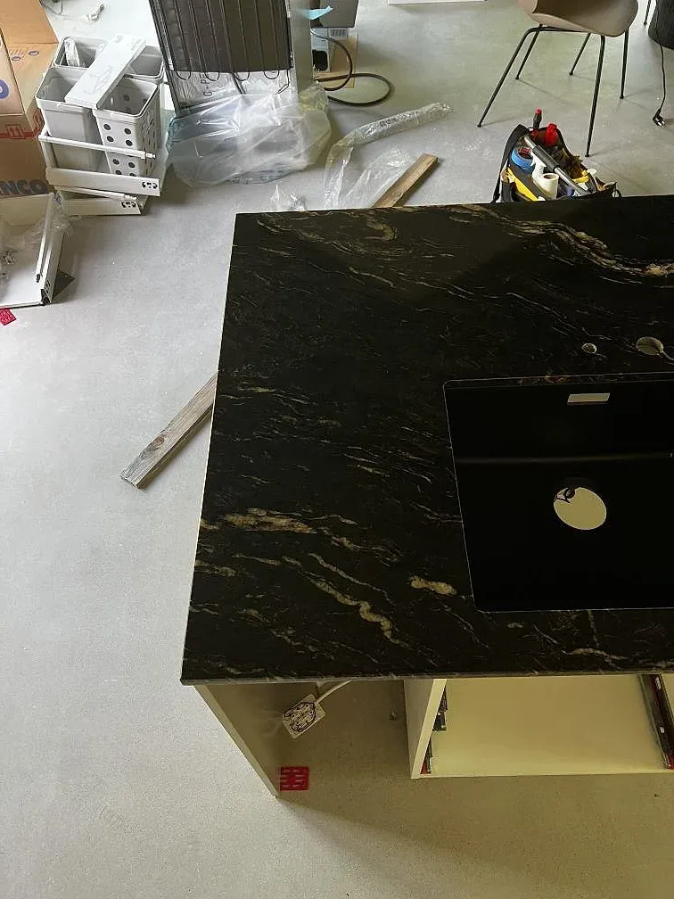 Köksö i polerad Cosmic Black granit med mörk yta och ljus ådring i ett kök under montering i Höganäs.