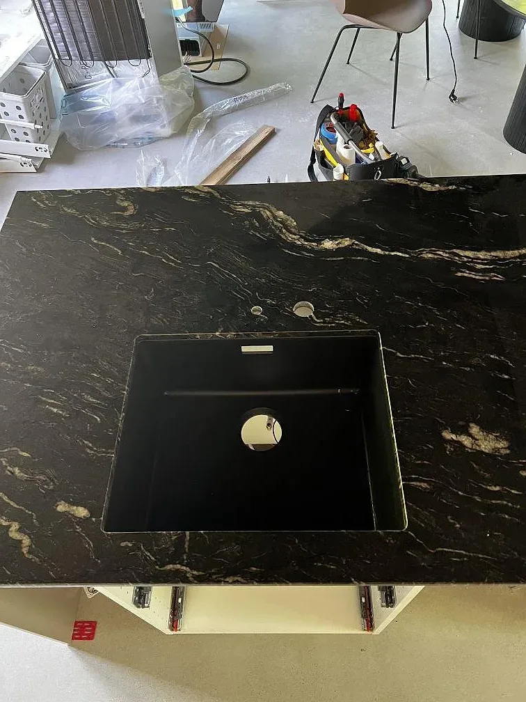 Polerad Cosmic Black granit med rektangulär öppning och borrade hål i en köksö under montering i Höganäs.