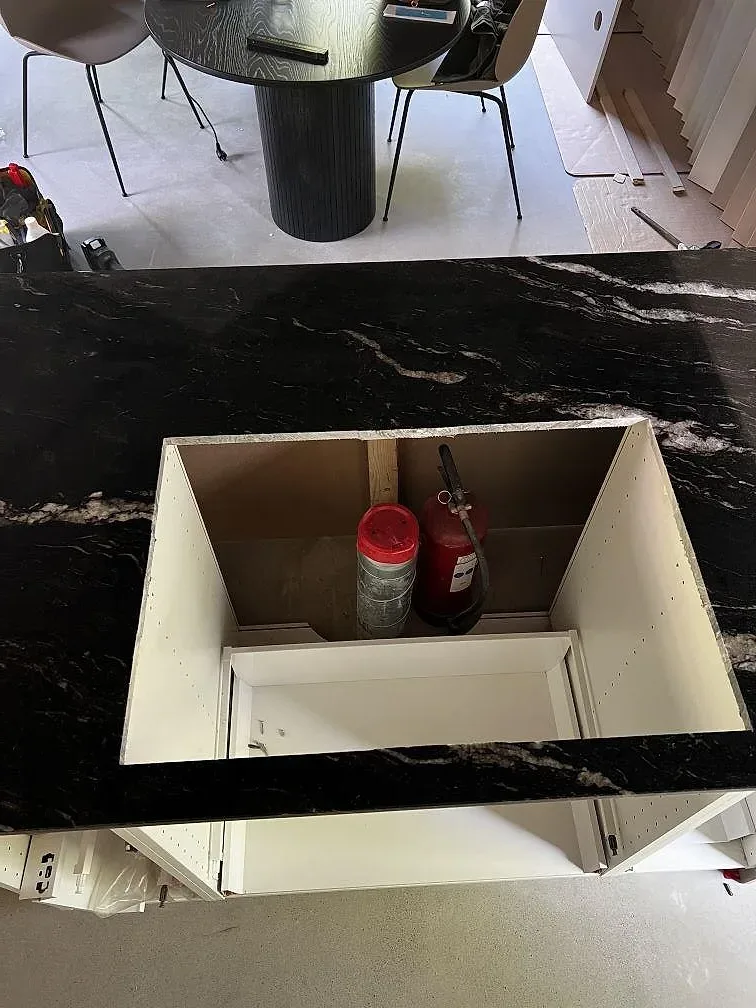 Polerad Cosmic Black granit runt en öppning i köksön med vita köksstommar under i Höganäs.