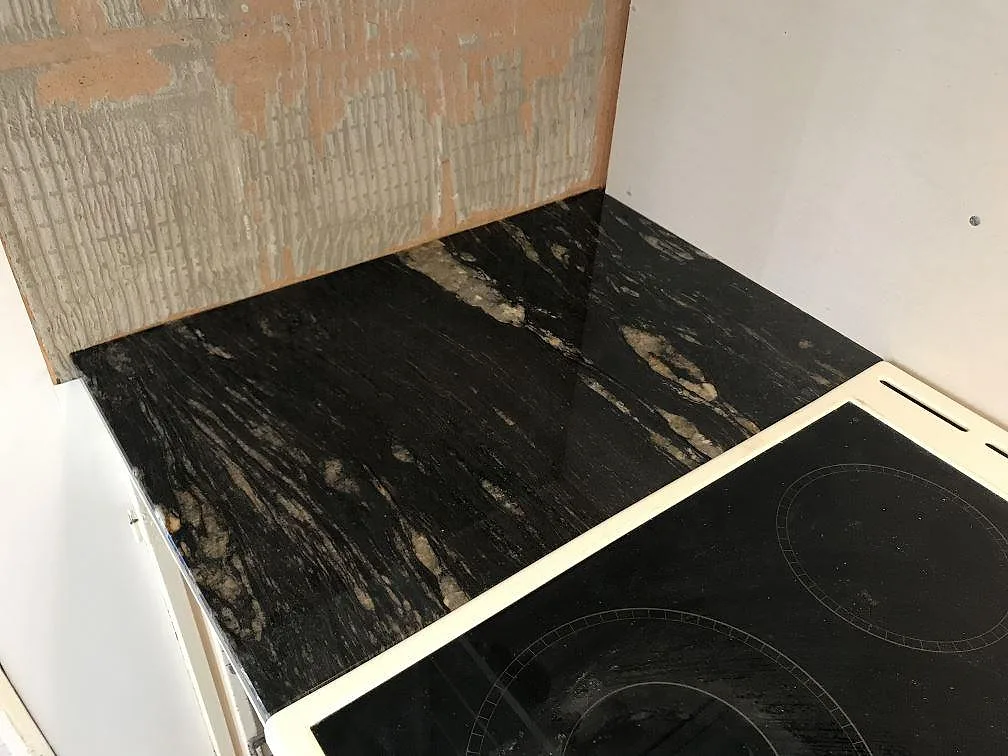 Köksbänkskiva i Cosmic Black granit med underlimmad diskho mot omålad vägg under montering i Hultsfred.