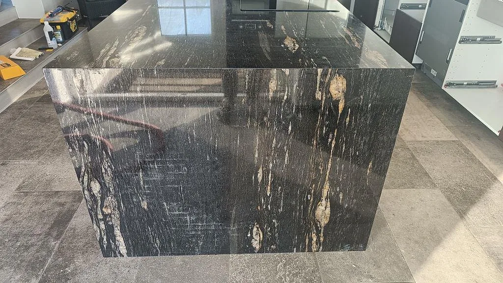 Närbild på den nedvikta gaveln på köksön i polerad Cosmic Black-granit med kopparbruna stråk i ett kök i Laholm.