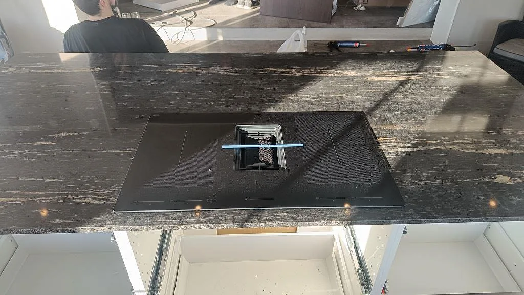 Polerad köksö i Cosmic Black-granit ovanifrån med induktionshäll och nedfälld fläkt i ett kök i Laholm.