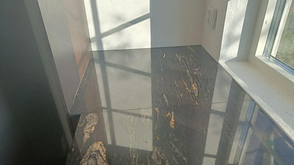 Polerad fönsterbänk i Cosmic Black-granit med varm guldådring intill ett fönster i ett kök i Laholm.