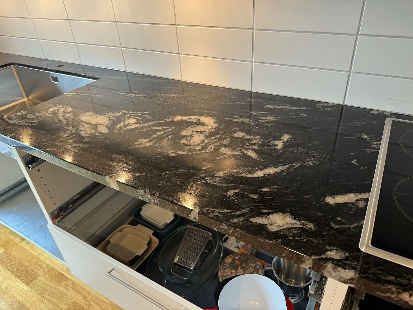 L-formad bänkskiva i Cosmic Black granit med vit kakelvägg, rostfri diskho och induktionshäll i Malmö.