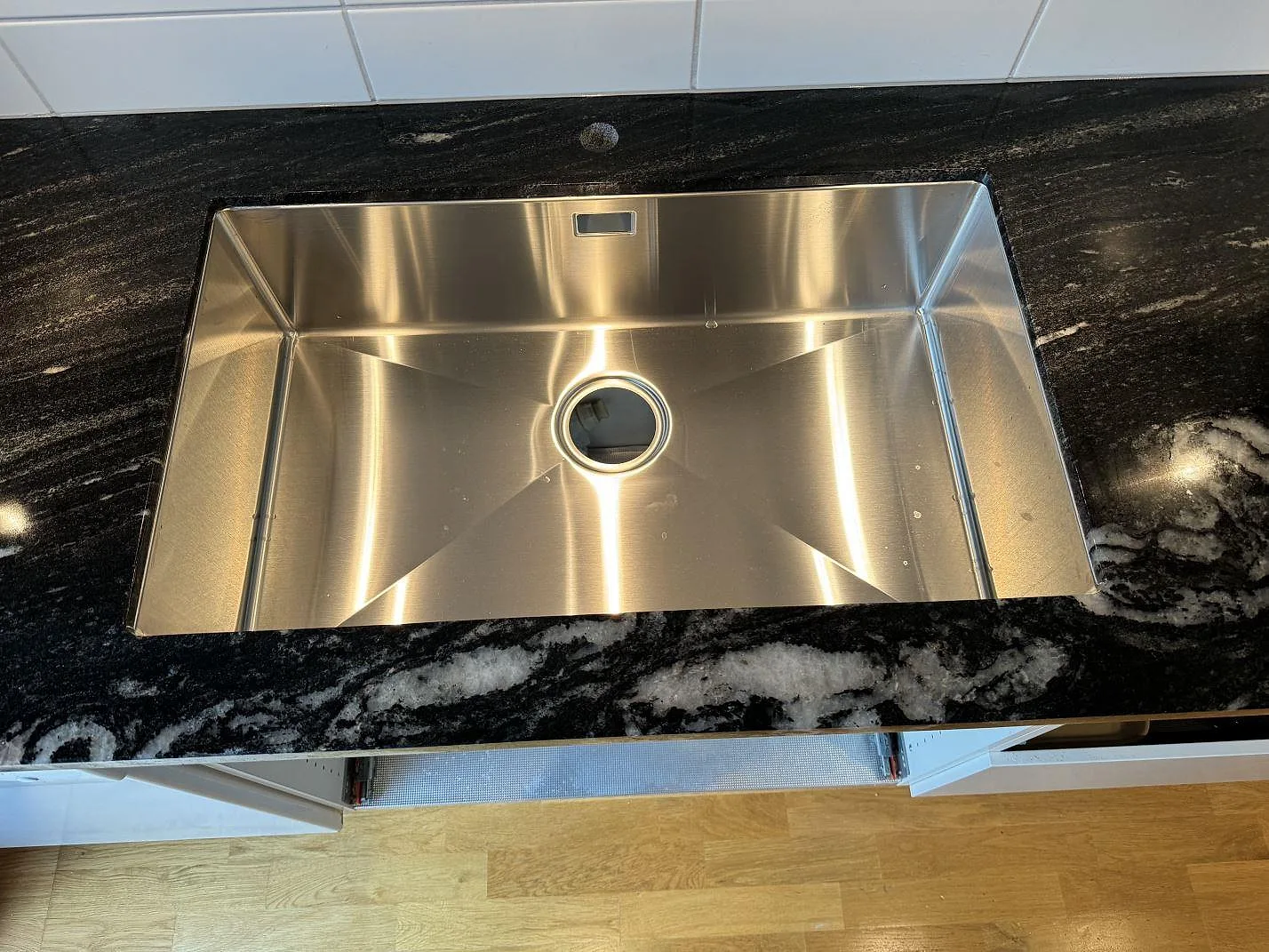 Underlimmad rostfri diskho i polerad Cosmic Black granit med mörk yta och ljus ådring i ett kök i Malmö.