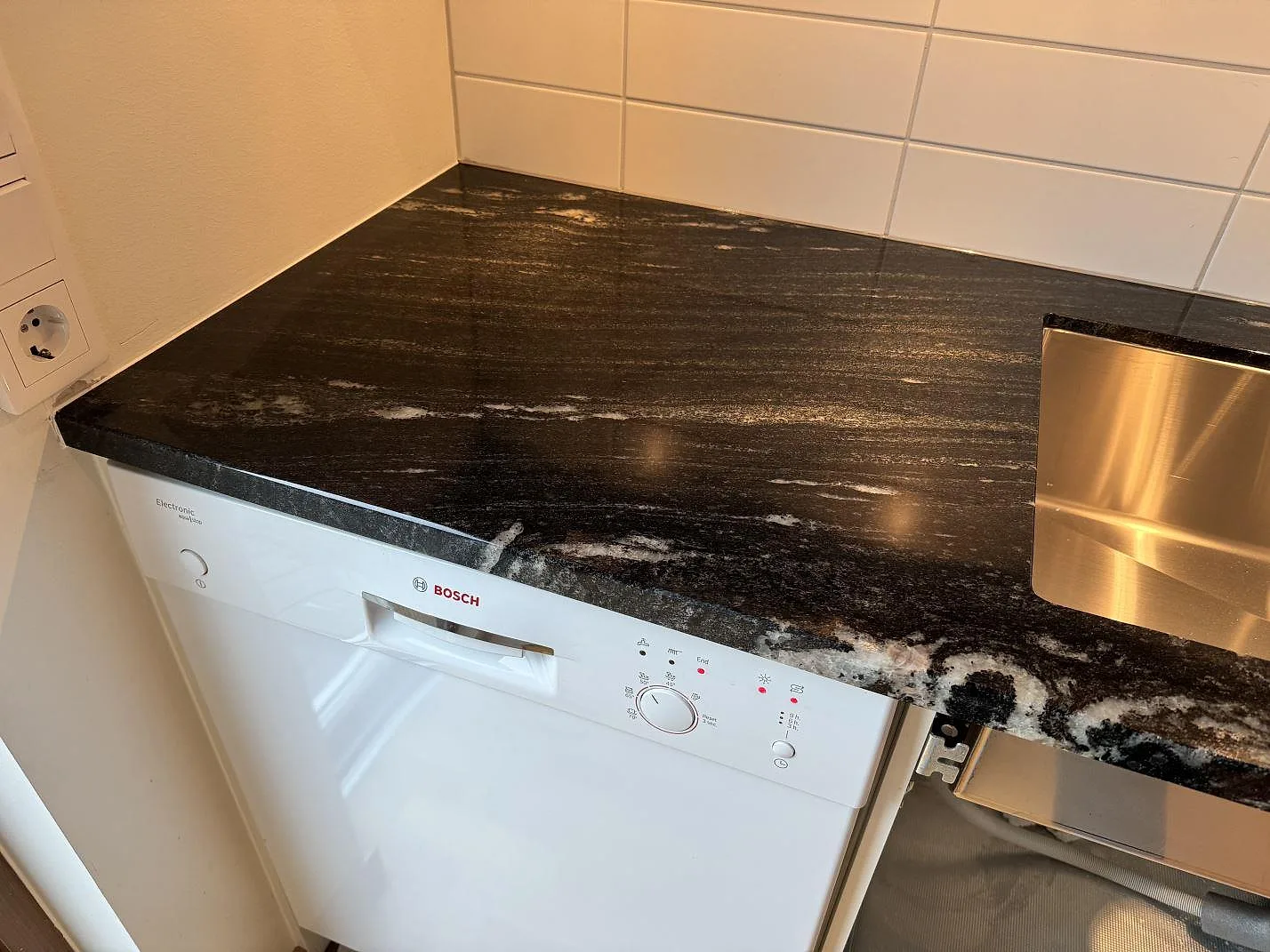 Polerad Cosmic Black granit vid diskbänk och diskmaskin, monterad på vit köksinredning i Malmö.