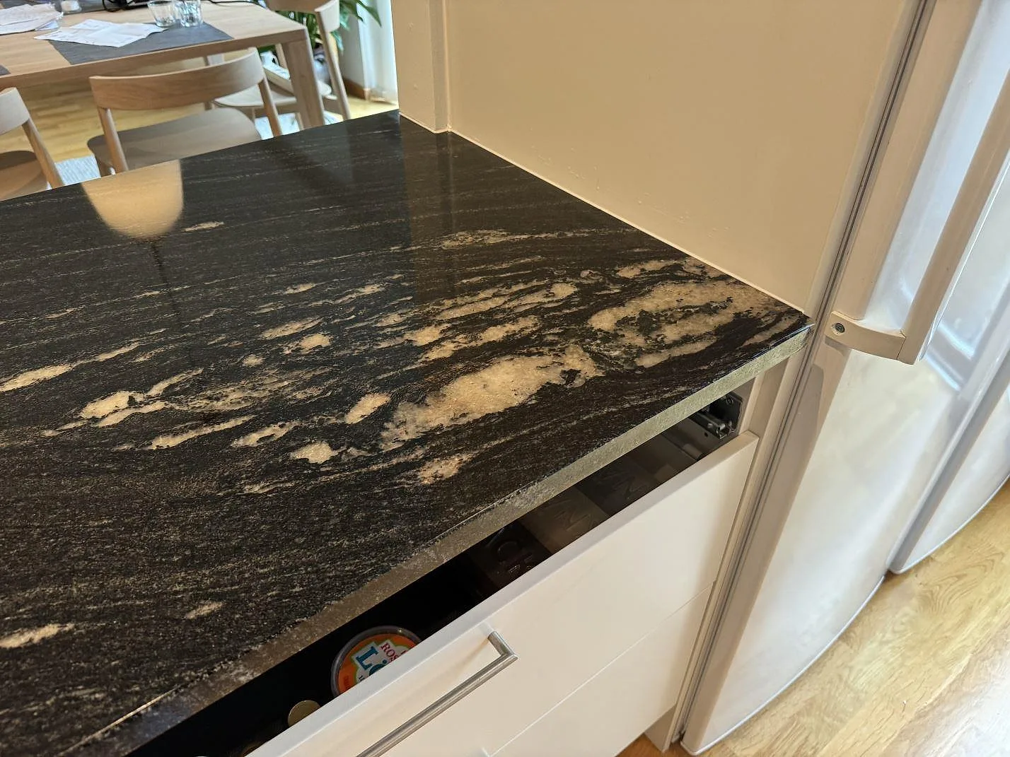 Detalj av polerad Cosmic Black granit med ljus ådring vid högskåp och kyl i ett kök i Malmö.