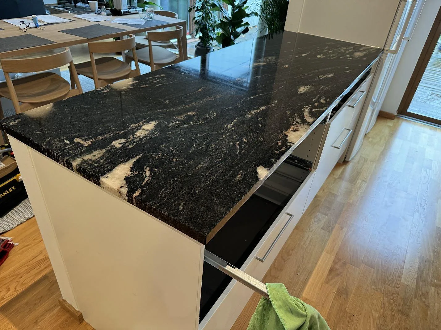 Lång köksbänkskiva i polerad Cosmic Black granit med ljus ådring på vita skåp i ett kök i Malmö.