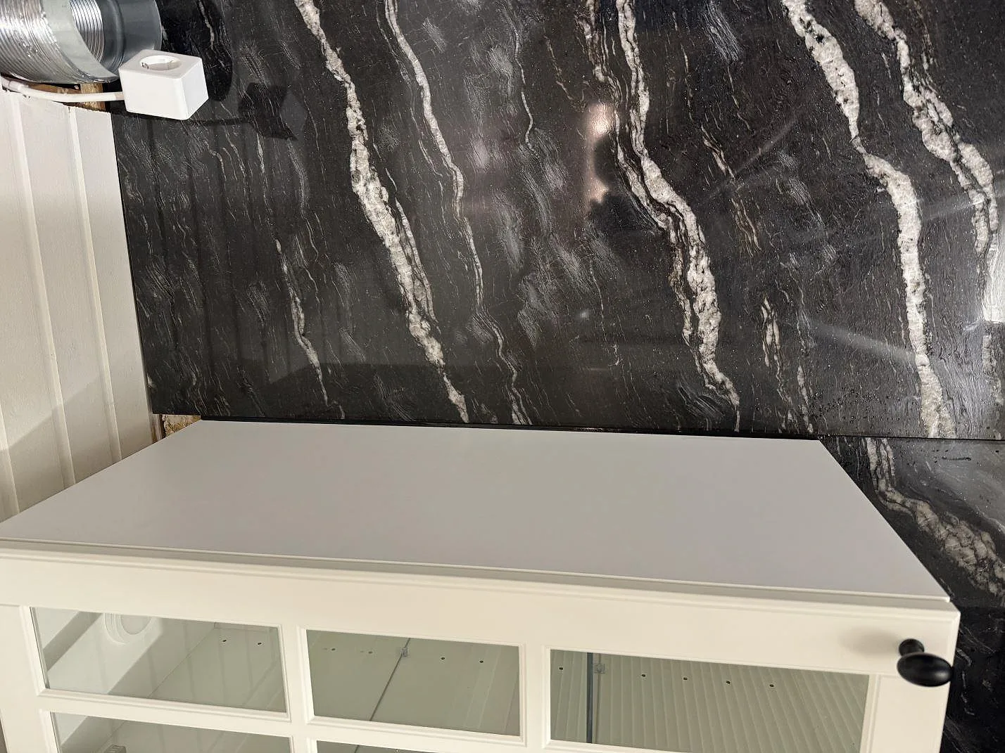 Väggbeklädnad i polerad Cosmic Black granit bakom vit köksinredning under montering i Malmö.