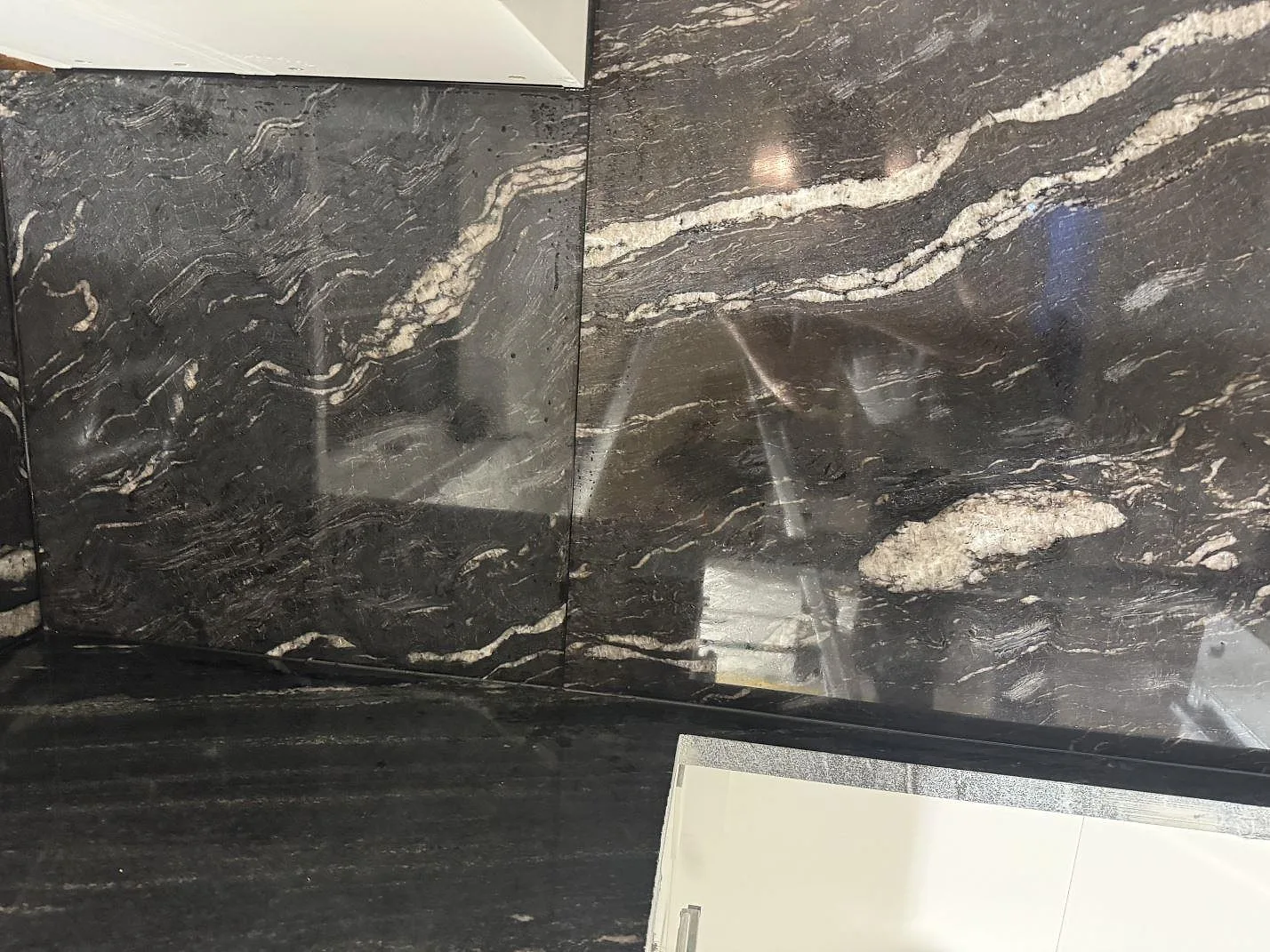 Detalj av polerad Cosmic Black granit där bänkskiva och väggpanel möts runt en öppning i ett kök i Malmö.
