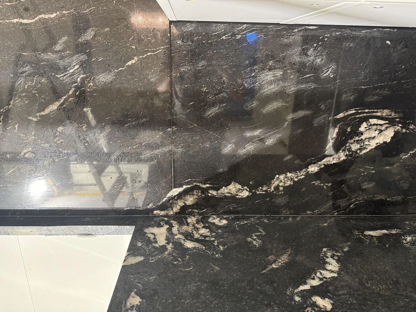 Närbild på blank Cosmic Black granit med ljusa ådror över bänkskiva och väggbeklädnad i Malmö.