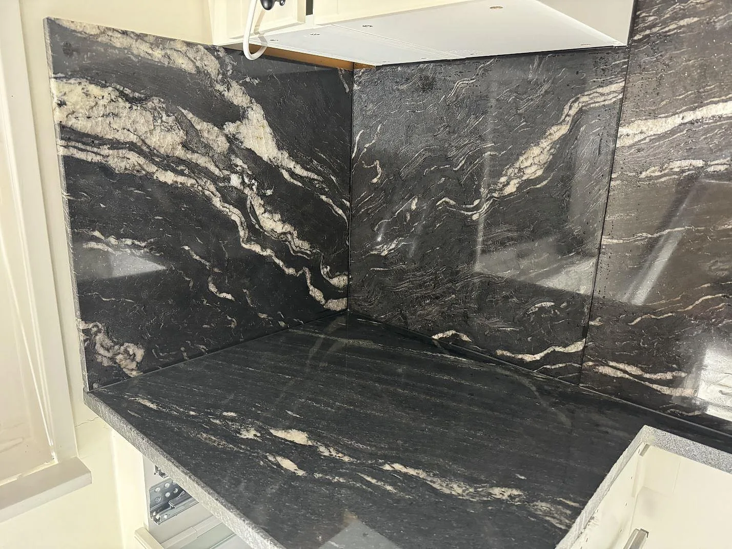 Köksbänkskiva i polerad Cosmic Black granit med matchande väggbeklädnad i ett vitt kök i Malmö.