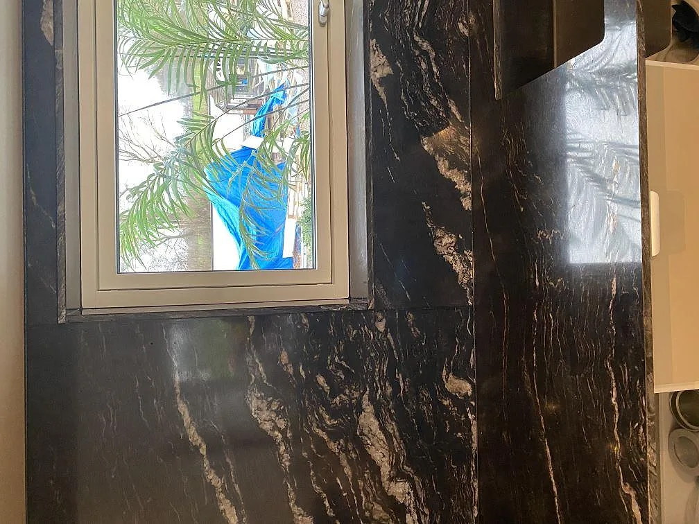 Fönsterparti omramat av Cosmic Black-granit som stänkvägg i ett kök under montering i Mörarp.