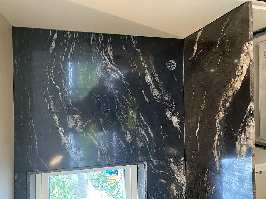 Heltäckande stänkvägg i Cosmic Black-granit kring ett fönster i ett kök i Mörarp, polerad yta med ljus ådring.