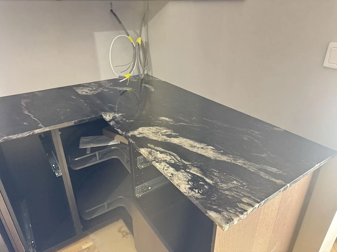 Köksbänkskiva i svart Cosmic Black-granit, polerad, monterad som L-bänk runt ett hörn med ljus ådring och kopparskimmer i ett kök i Sölvesborg.