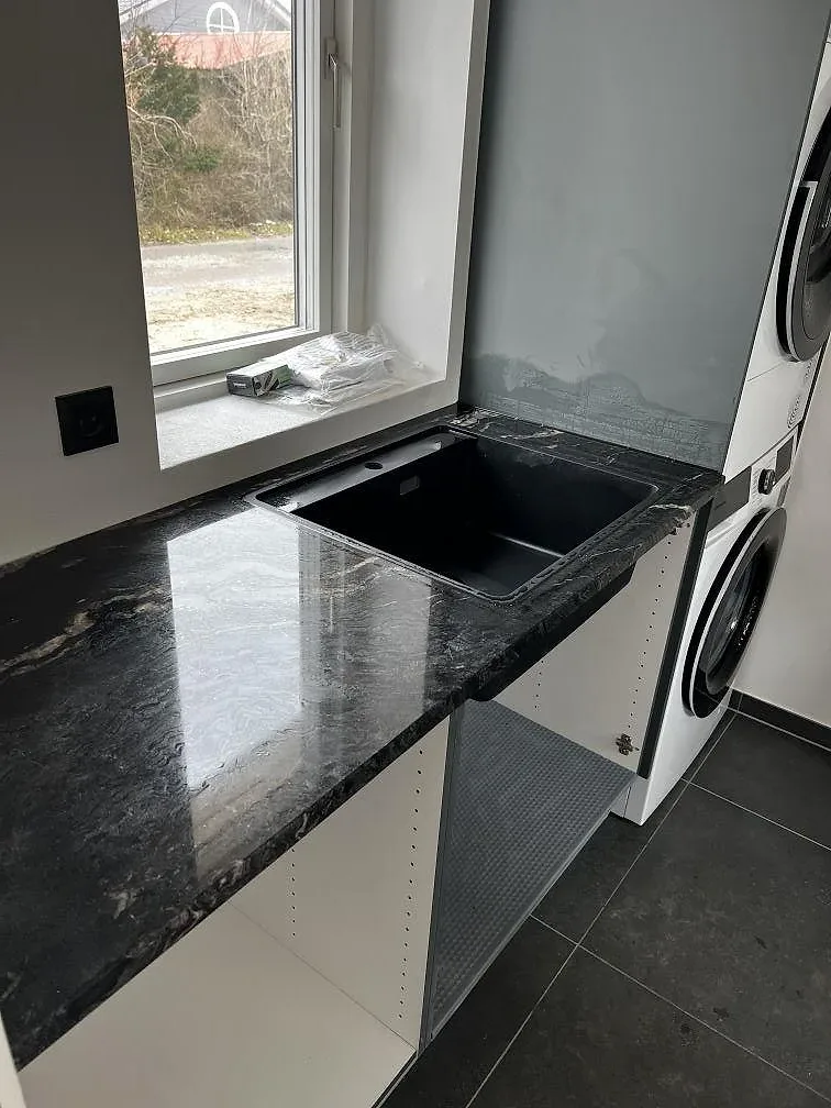 Köksbänkskiva i svart Cosmic Black granit, polerad med ljus ådring, med underlimmad svart diskho vid fönstret i ett kök i Solrød Strand.