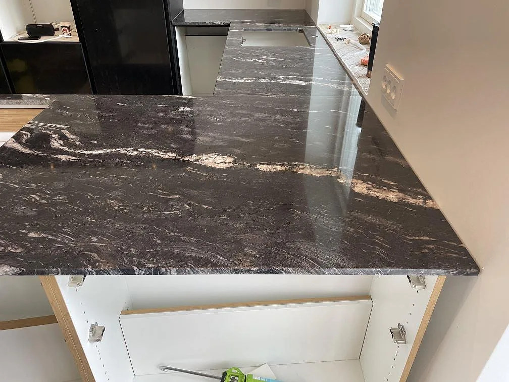 Närbild av polerad Cosmic Black granit på köksö med ljus ådring och öppna köksstommar i Tølløse.
