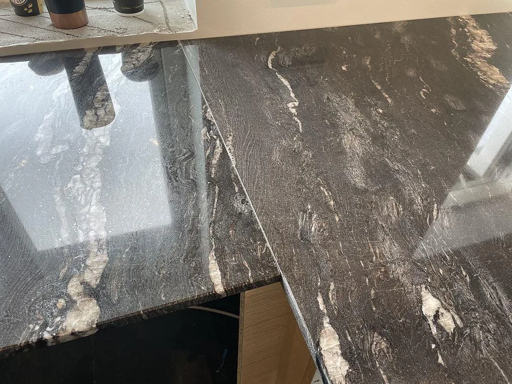 Detalj av skarv och blank polerad Cosmic Black granit med vit ådring i köket i Tølløse.