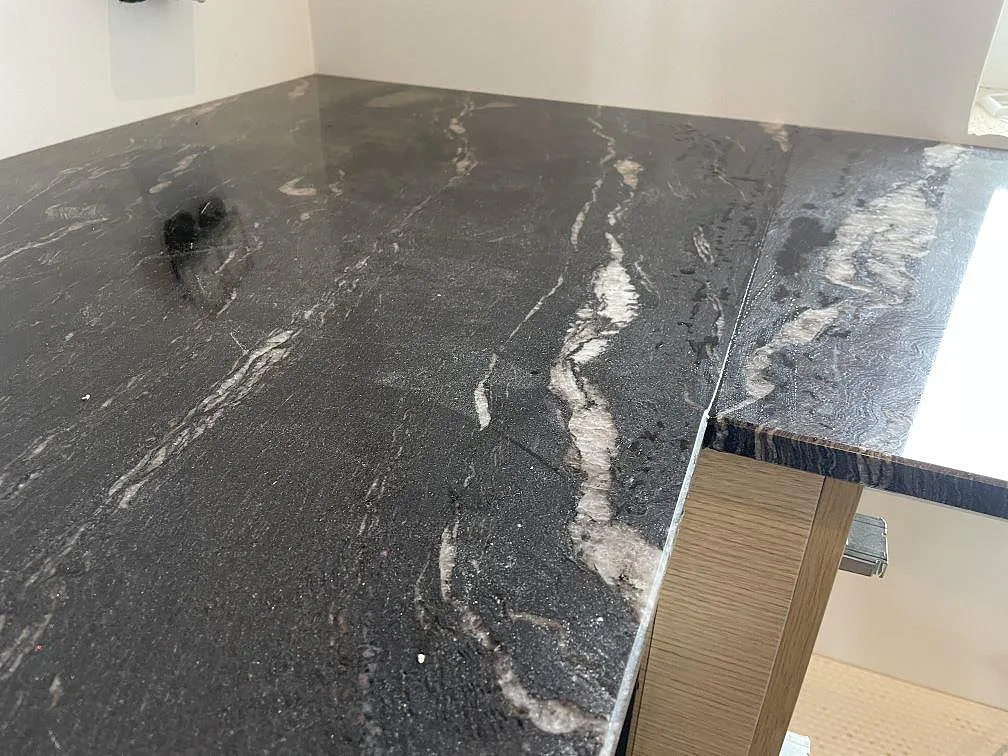 Närbild av 20 mm polerad Cosmic Black granit med profilerad kant och ljus ådring i Tølløse.