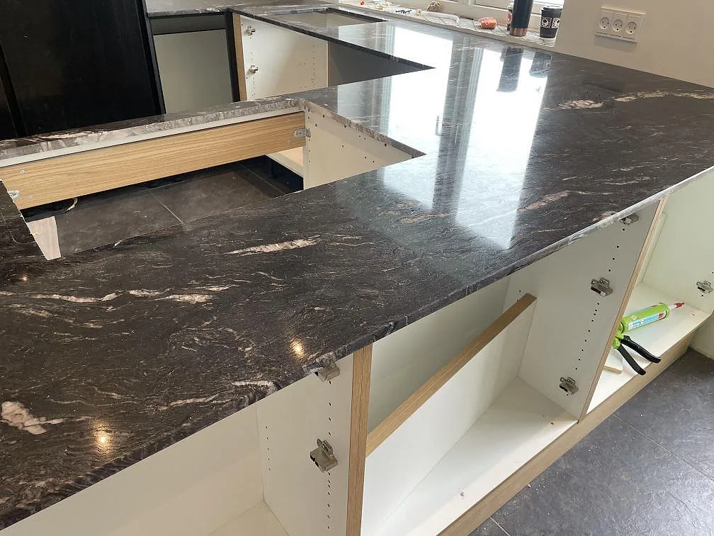 Polerad köksbänkskiva i Cosmic Black granit med tydlig vit ådring, diskho och hällurtag under montering i Tølløse.