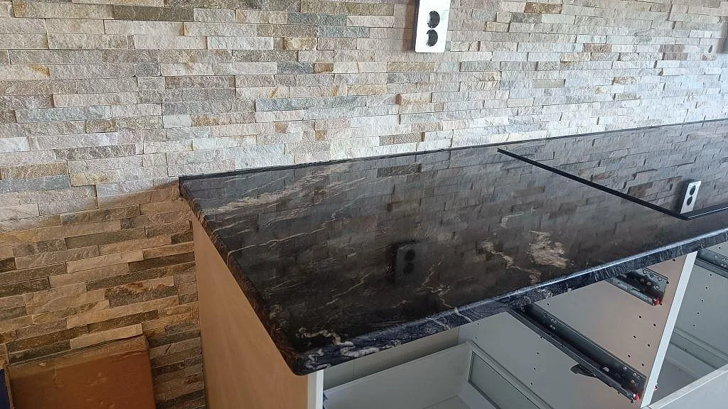 Rak köksbänk i Cosmic Black-granit sedd snett ovanifrån under montering, med tydlig flödande ådring i den svarta polerade stenen i Trollhättan.