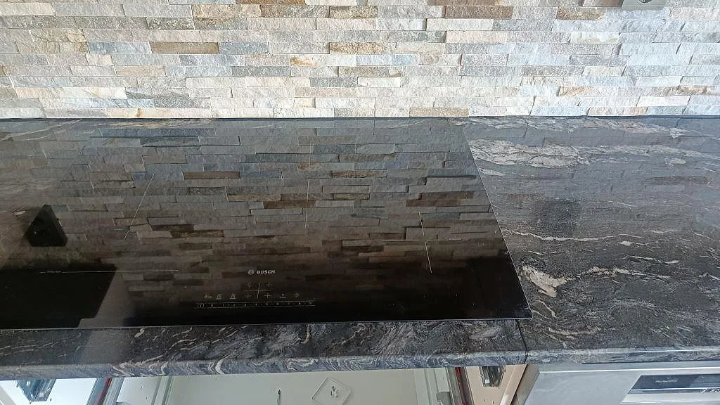 Polerad Cosmic Black-granit med infälld Bosch induktionshäll, där den grå och kopparfärgade ådringen syns tydligt i köksbänken i Trollhättan.