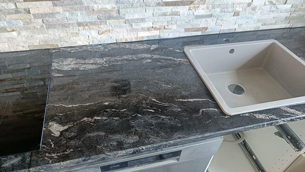 Ljus underlimmad diskho monterad under bänkskivan i svart Cosmic Black-granit i ett kök i Trollhättan.