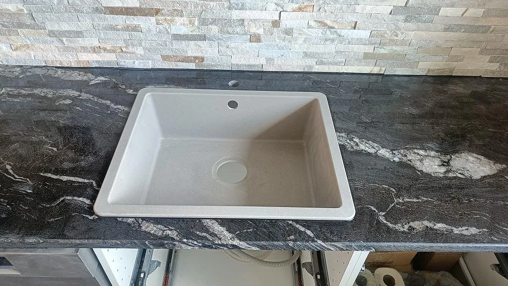 Närbild på ljus underlimmad diskho i polerad Cosmic Black-granit med kopparton ådring i ett kök i Trollhättan.
