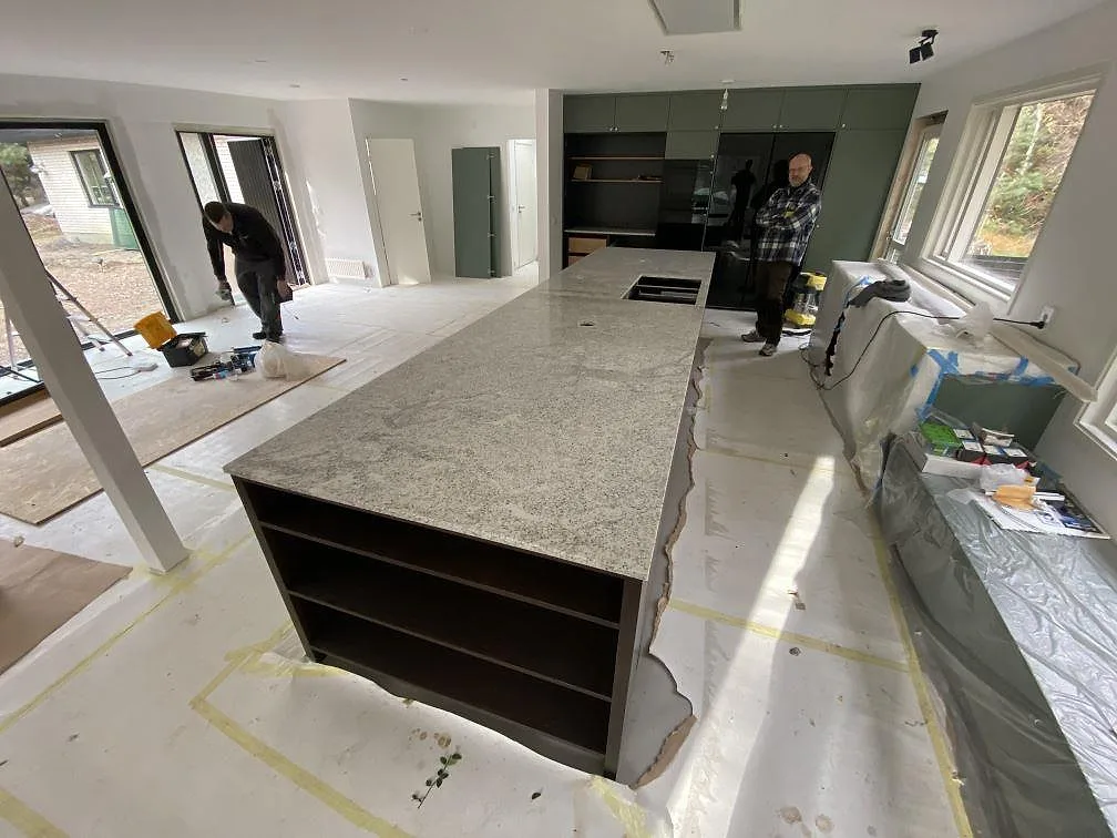 Köksbänkskiva och köksö i Cotton White granit, vit med gråspräckligt korn, monterad i ett ljust kök under installation i Höllviken.