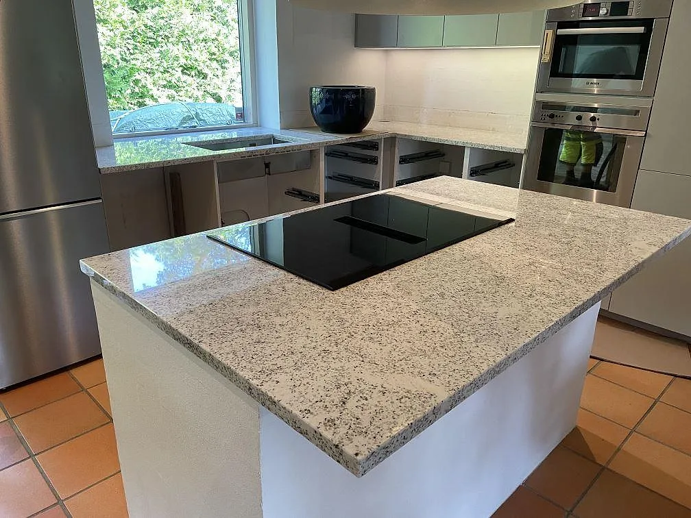 Köksbänkskiva i 30 mm polerad Cotton White granit med stor köksö, svart induktionshäll och terrakottafärgat golv i Höllviken.