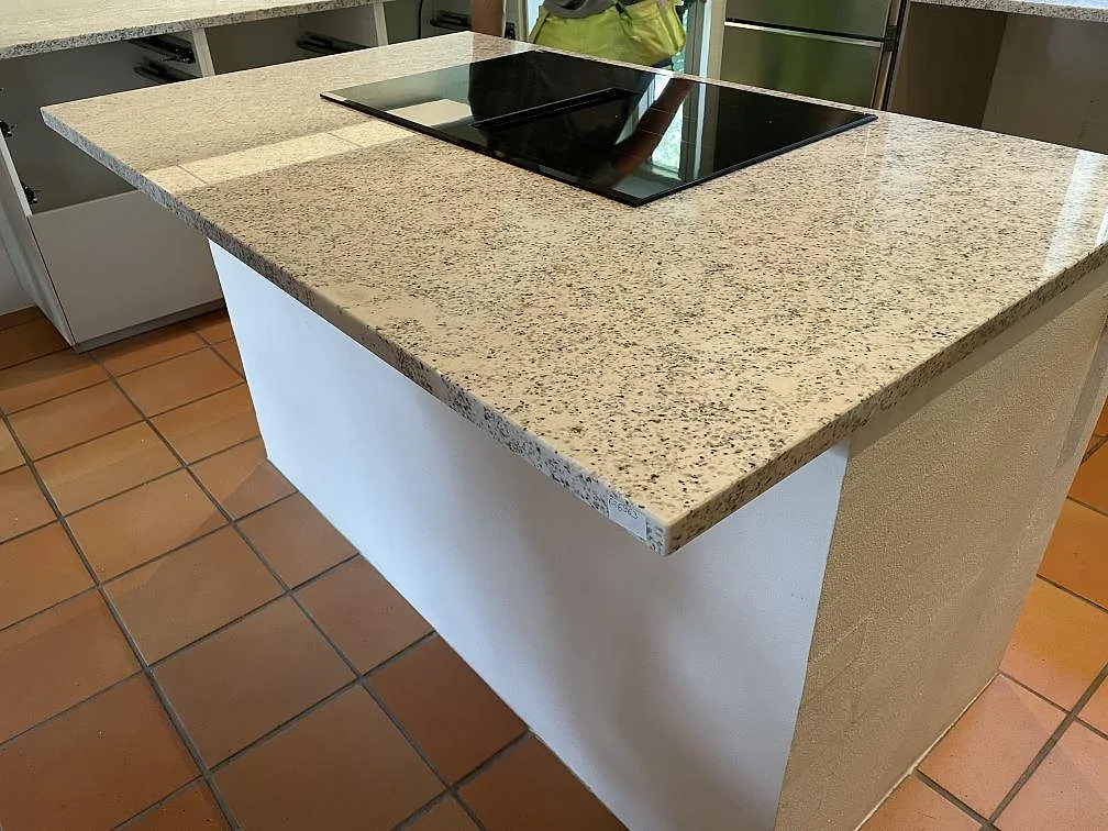 Närbild på köksö i Cotton White granit, polerad 30 mm skiva med svart induktionshäll och markerad stenkant i Höllviken.