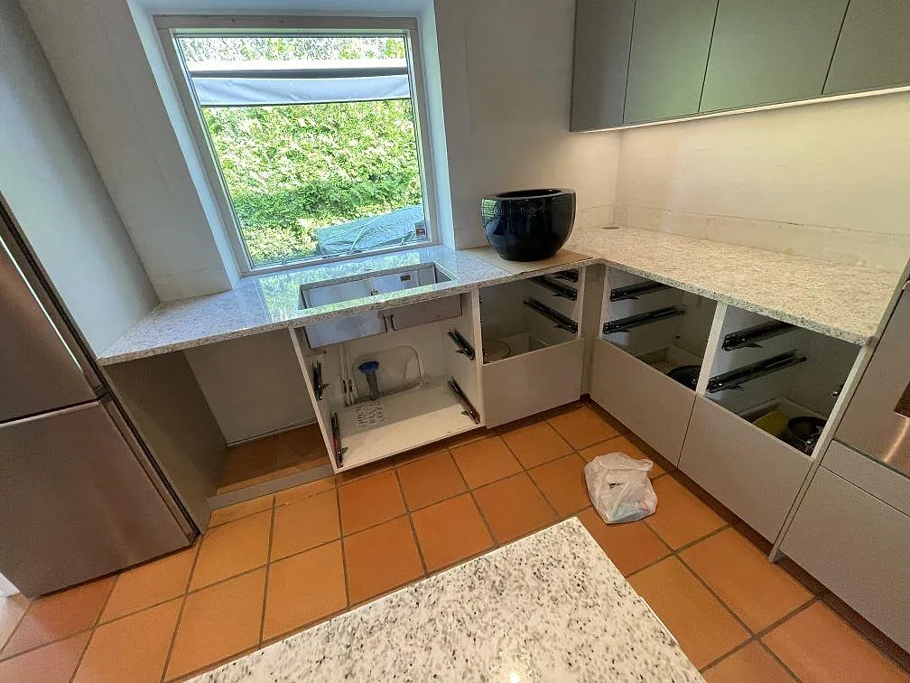 Väggbänkar i Cotton White granit med underlimmad diskho vid fönster och vita köksstommar under montering i Höllviken.