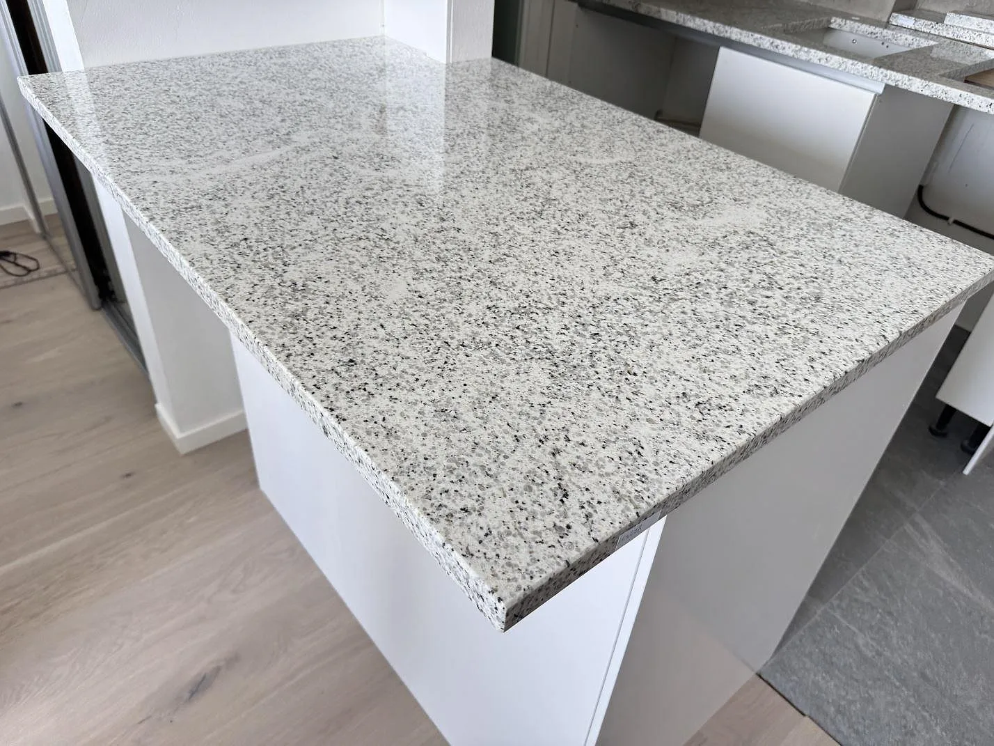 Köksbänkskiva i polerad Cotton White granit på en större bänkdel i ett kök under montering i Lomma.