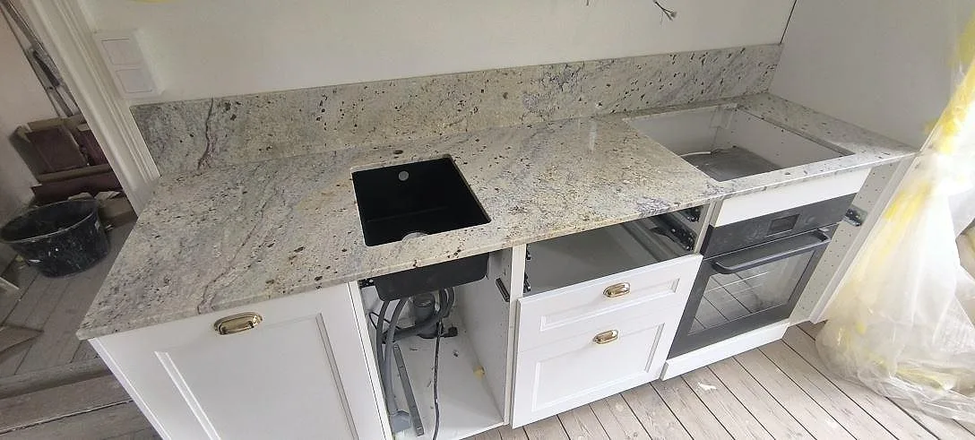 Ovanifrånvy av polerad Cotton White granit med svart diskho, hällöppning och kornig ljus yta i ett kök i Stockholm.