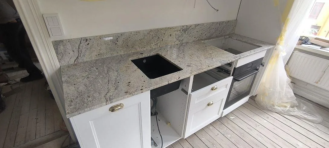 Polerad köksbänkskiva i Cotton White granit med svart diskho, hällurtag och matchande stänkskydd i ett kök i Stockholm.