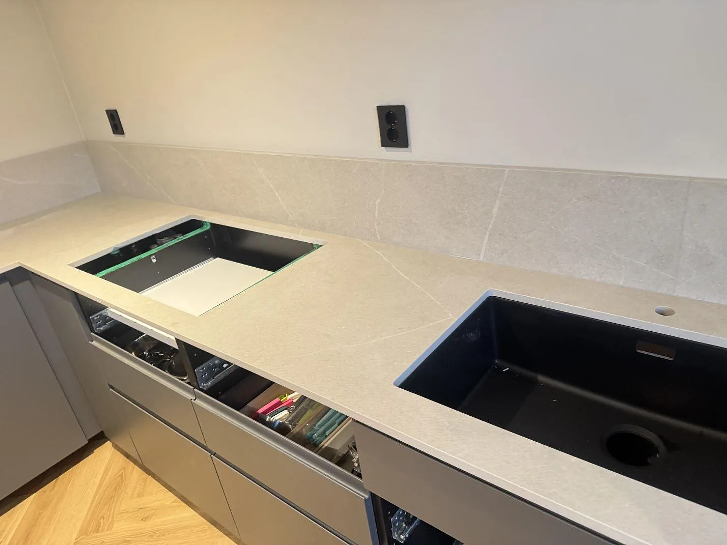 Köksbänkskiva i beige Dekton Adia, matt 20 mm keramik, med låg stänkkant, mörk diskho och hällurtag i Stenungsund.