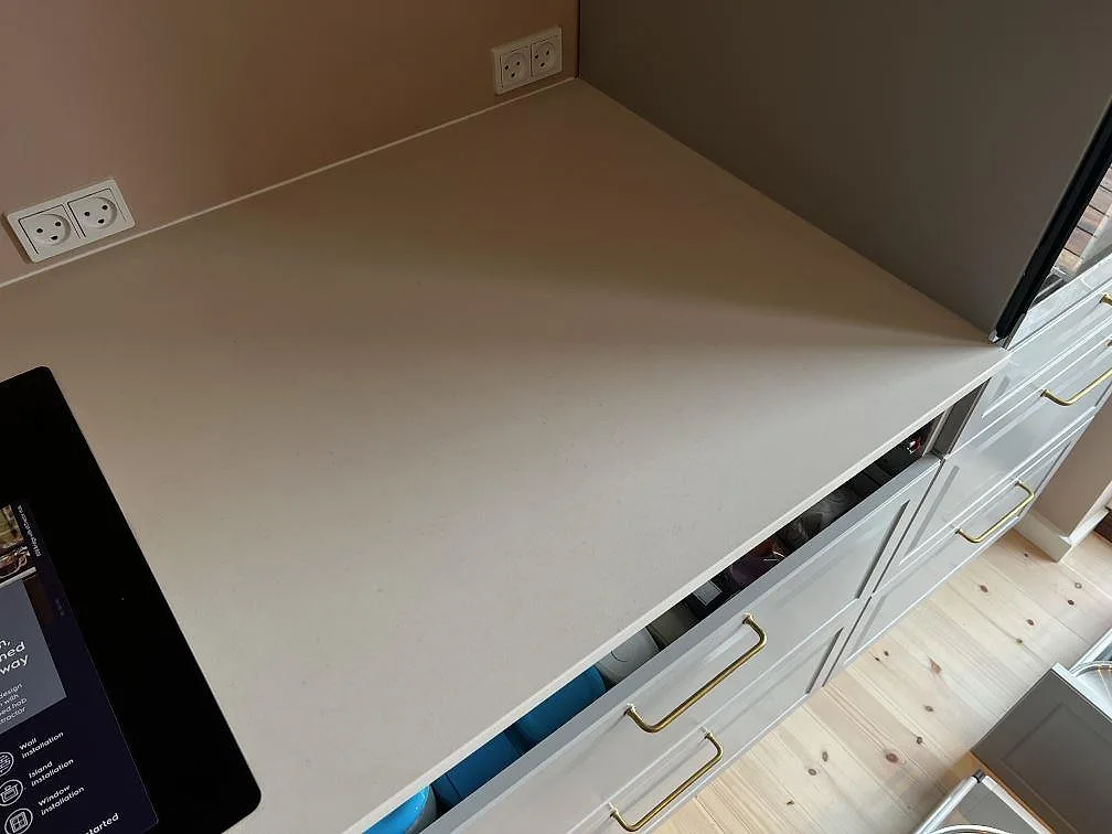 Ljus arbetsyta i matt Dekton Aeris keramik med vägguttag, skåpsfront och träfönsterdetalj i ett kök i Kgs. Lyngby.
