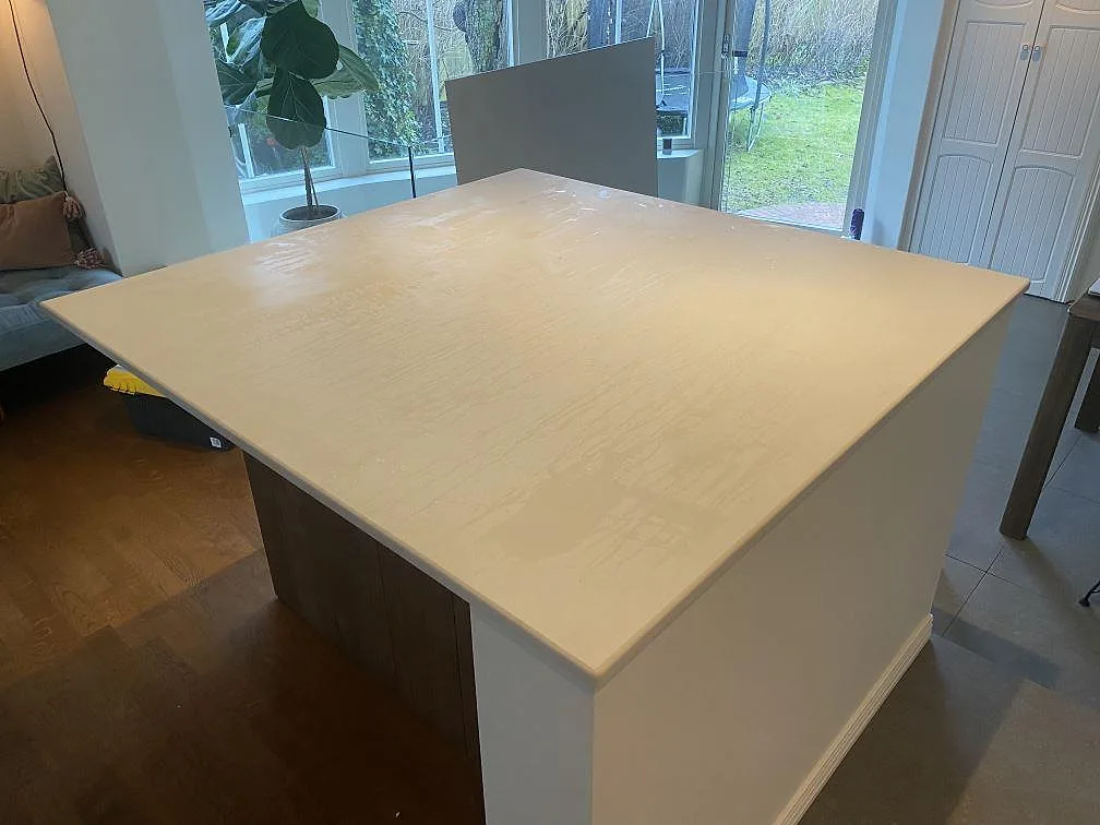 Köksö med matt köksbänkskiva i ljus Dekton Aeris, monterad ovanpå en stomme med träfront i ett kök i Limhamn.