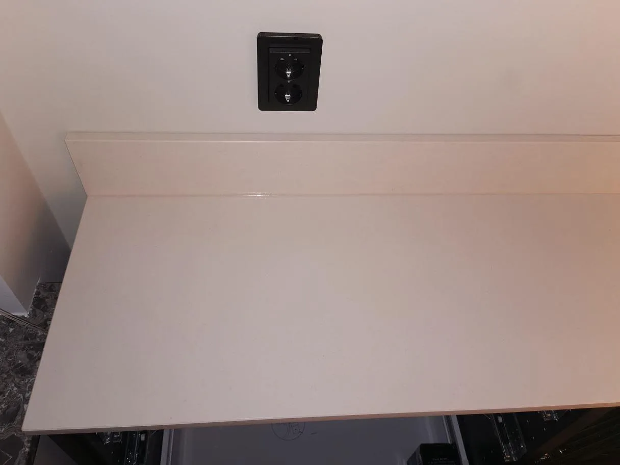 Installerad köksbänkskiva i matt vit Dekton Aeris med uppvikt stänkkant ovanför lådstommar i ett kök i Lund.