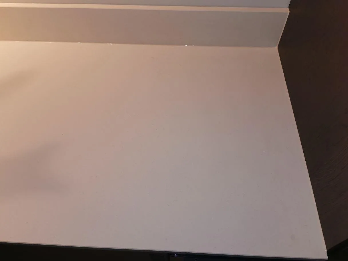 Köksbänkskiva i matt vit Dekton Aeris med uppvikt stänkkant och eluttag i ett kök i Lund.