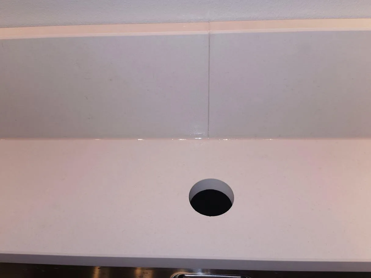 Blandarehål och uppvikt stänkkant i matt vit Dekton Aeris köksbänkskiva i ett kök i Lund.