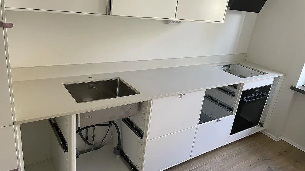 Matt köksbänkskiva i ljus Dekton Aeris, keramik, med rostfri diskho, stänkkant och hällurtag i ett kök i Malmö.