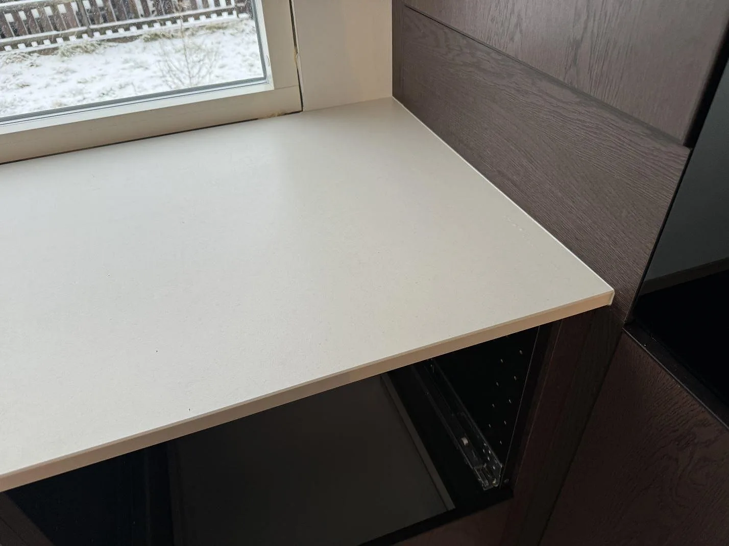 Detalj av matt Dekton Aeris vid fönster och högskåp i ett kök med mörk träinredning i Mariestad.