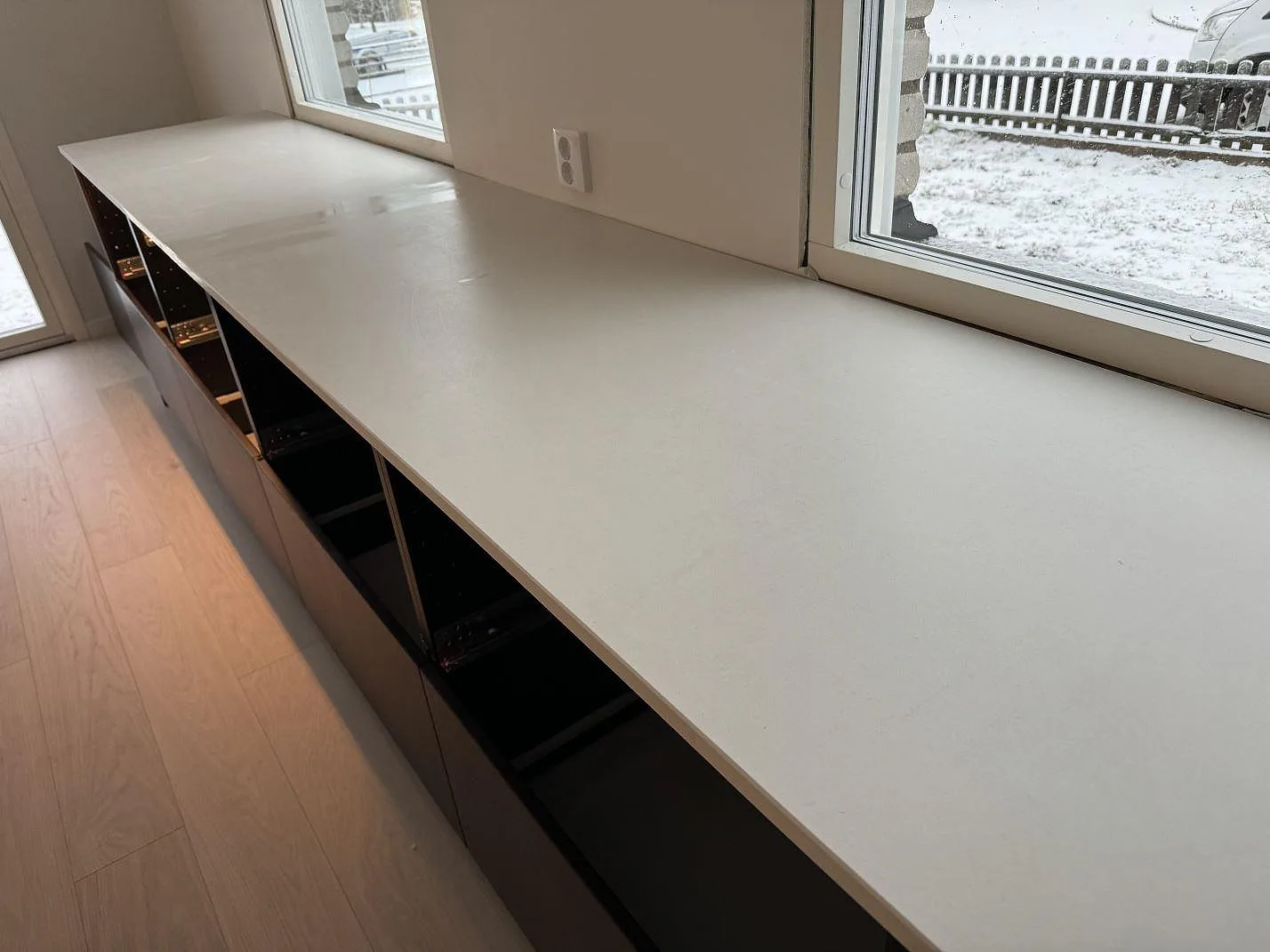 Ljus köksbänkskiva i matt Dekton Aeris längs fönsterväggen med mörka stommar i Mariestad.